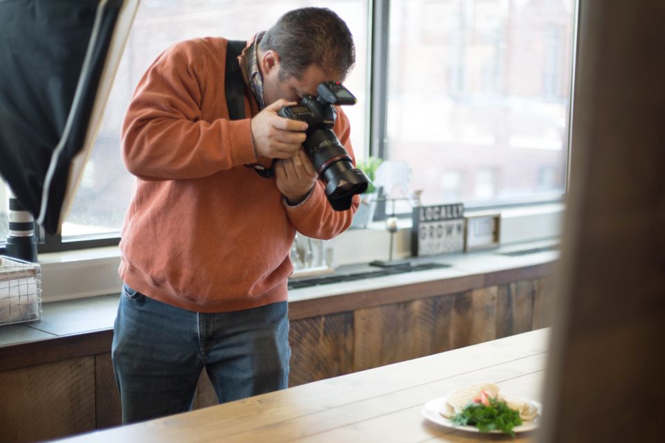 A photographer shoots a plated dish on a restaurant counter by a window.