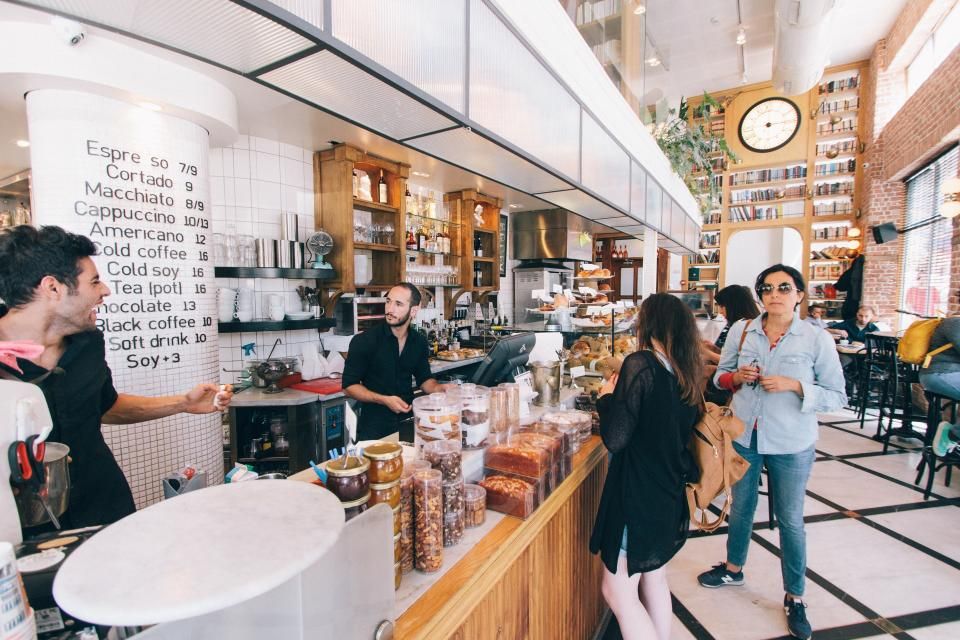 Des employés derrière le comptoir d’un café servent des clients, un menu écrit sur un pilier.